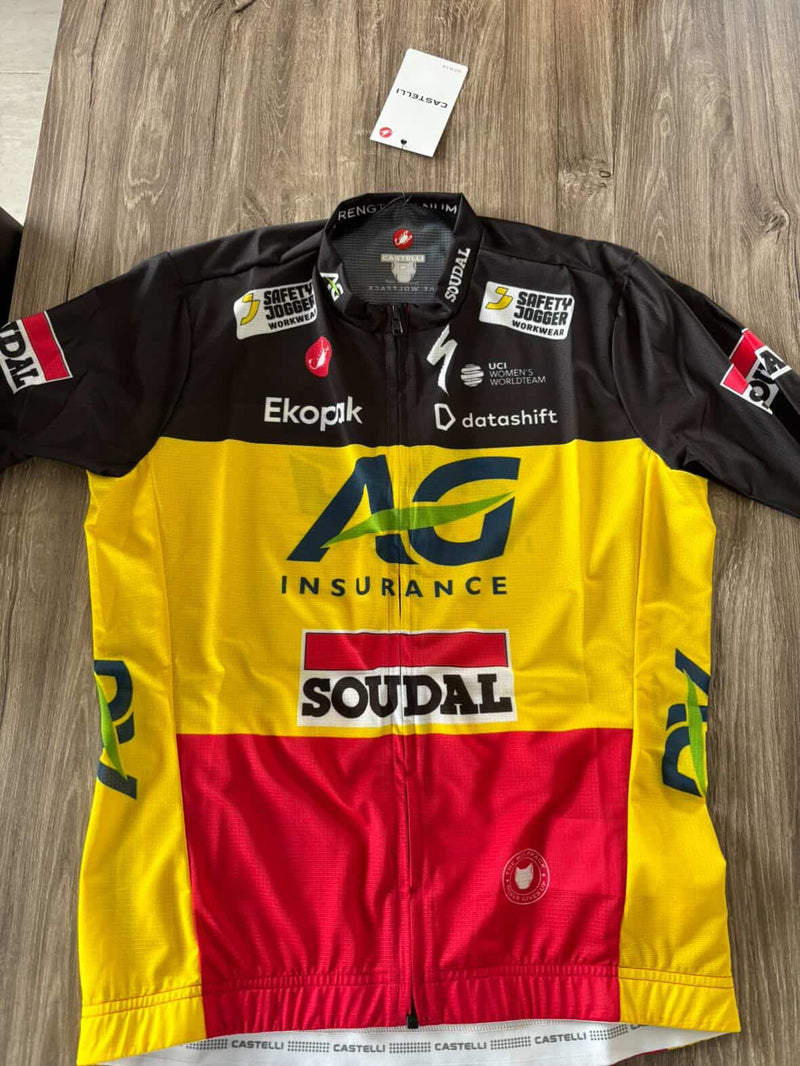 Top down shot of the Belgian National cycling jersey with multiple brand logos on a wooden surface.