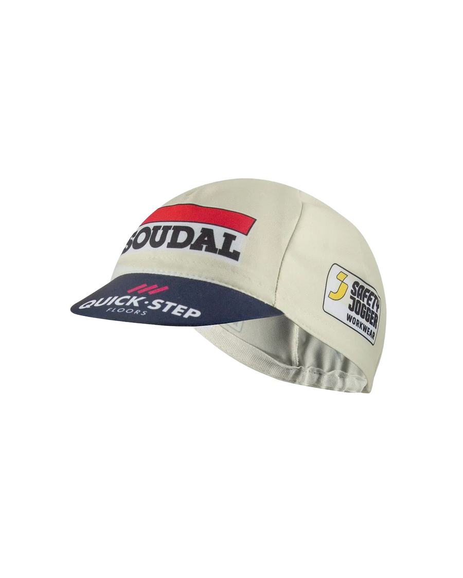 A cycling cap, shot from a slight side angle, in light beige with a navy blue brim, featuring the red and navy Soudal logo on the front and a Quick-Step logo on the brim, alongside a Safety Jogger Workwear logo on the side. Displayed on a white background. 