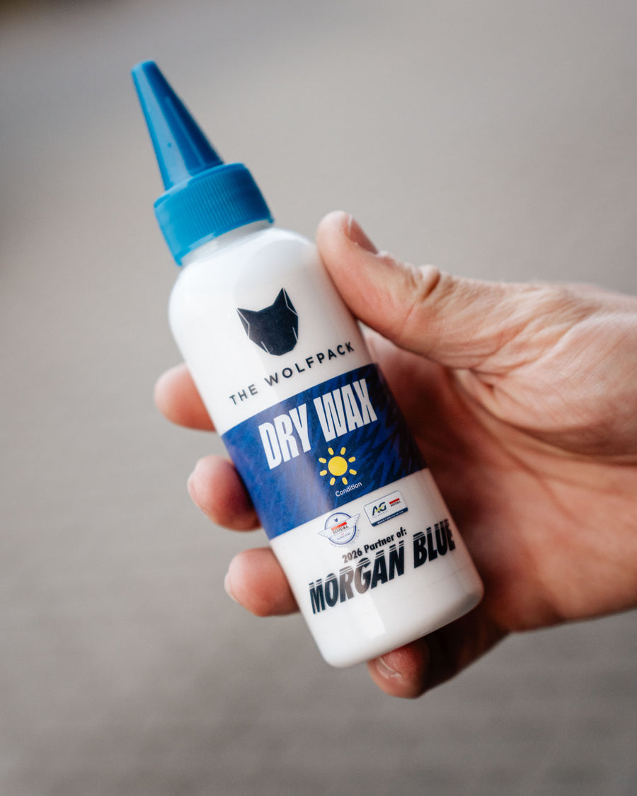 Hand holding a bottle of 'Dry Wax' by The Wolfpack and Morgan Blue with a gray background.