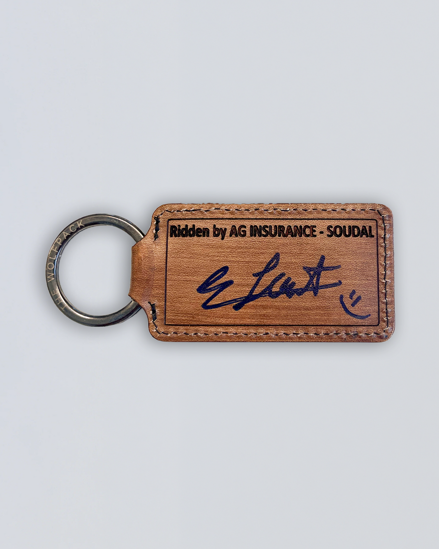 Brown leather keychain with text and Kim Le Court signature on a light gray background.
