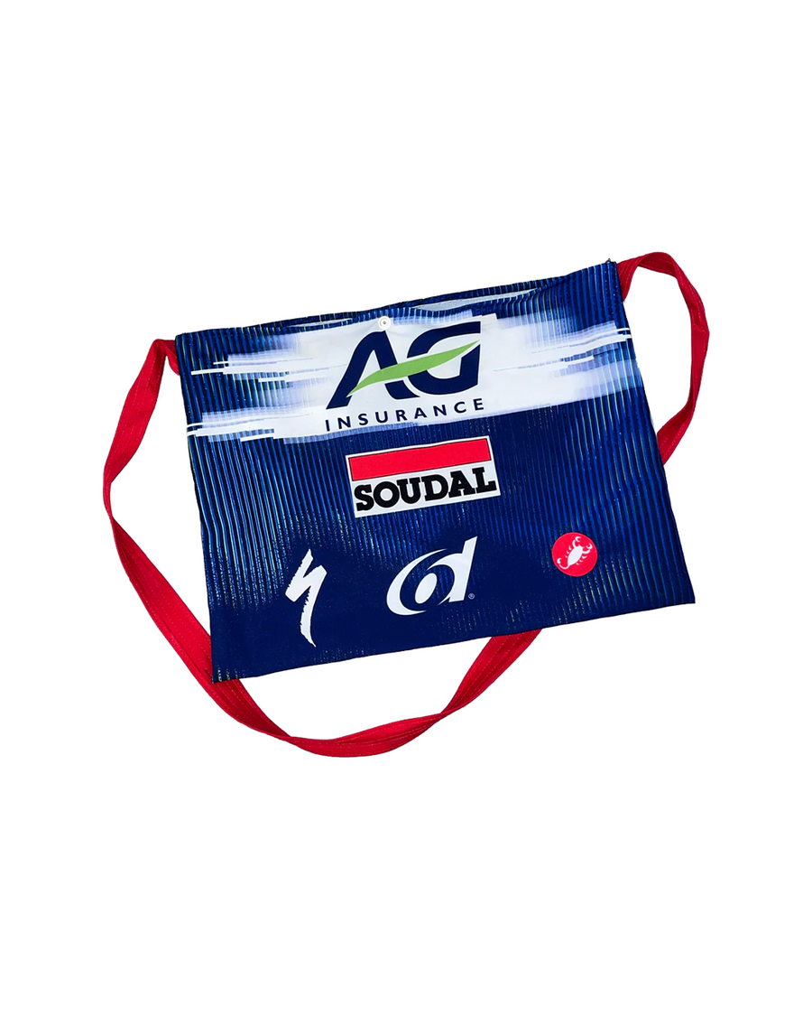 A blue and whitemusette featuring sponsor logos including AG Insurance, Soudal, Specialized, 6d and Castelli, with red straps, shown on a plain white background.
