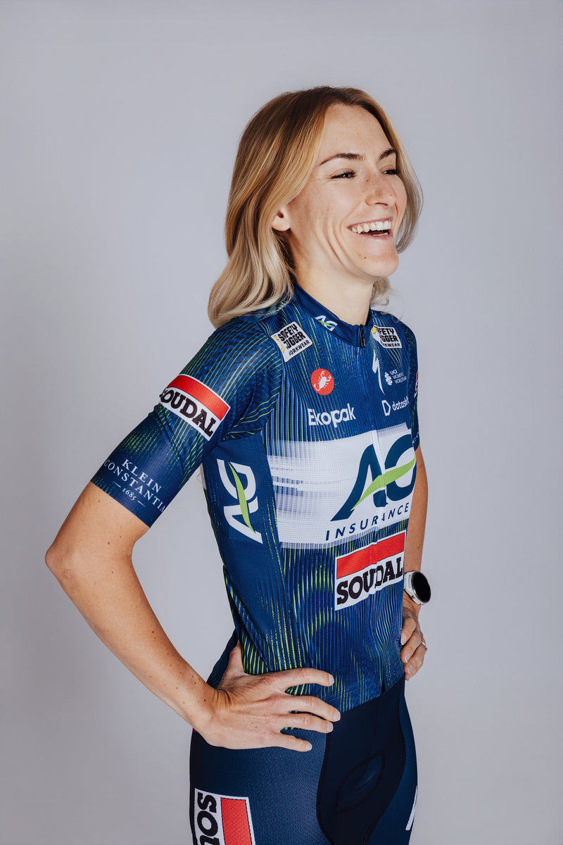 Person wearing a blue cycling jersey with various sponsor logos on a plain background