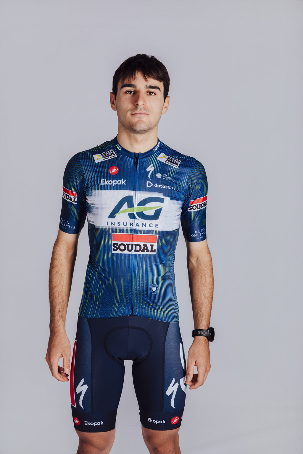 Cyclist wearing a blue cycling jersey with various sponsor logos on a gray background
